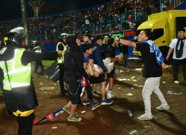 Supporters evacuate a man due to tear gas fired by police during the riot after the football match between Arema vs Persebaya at Kanjuruhan Stadium