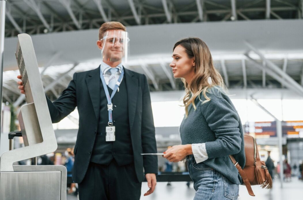 Employee helping to use terminal. Young female tourist is in the airport at daytime Employee helping to use terminal. Young female tourist is in the airport at daytime