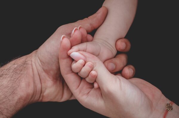 Woman and man holding newborn baby’s hand Woman and man holding newborn baby’s hand